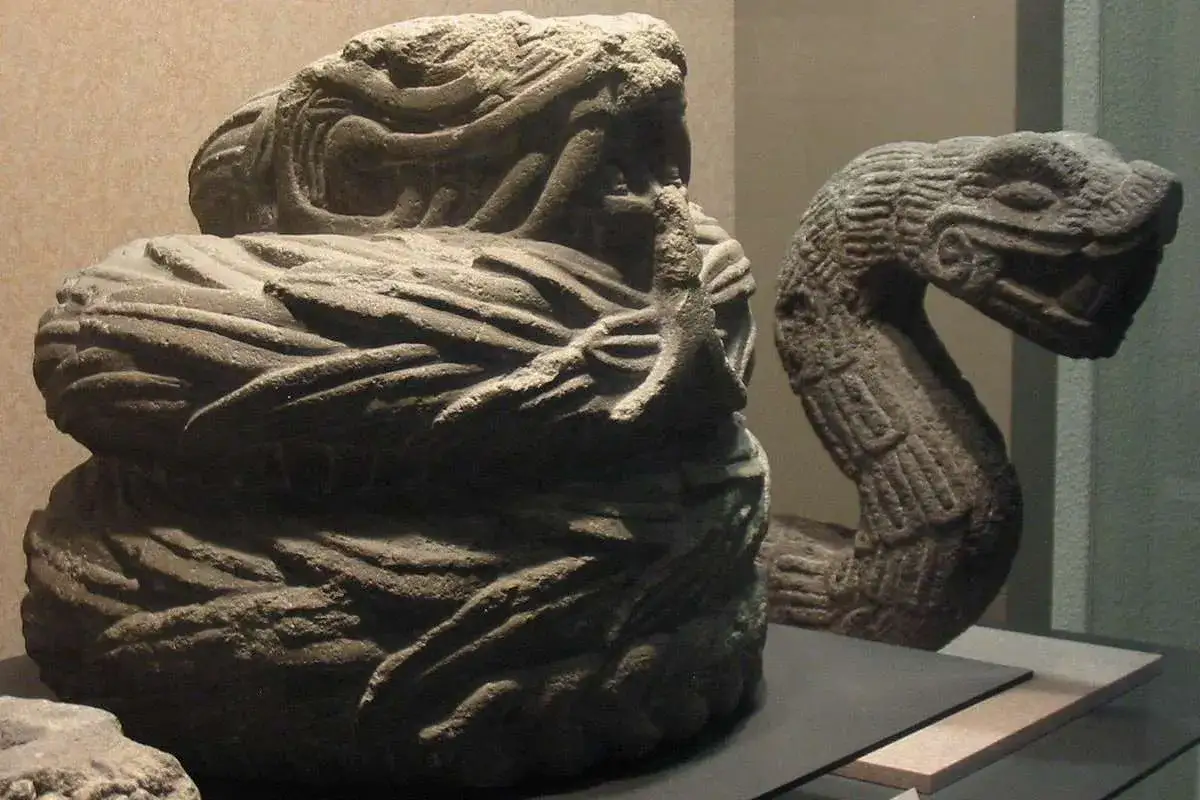 Antiche sculture in pietra raffigurano l'ascesa della divinit&agrave; dei serpenti, con un serpente arrotolato in primo piano e un altro che si protende sullo sfondo.
