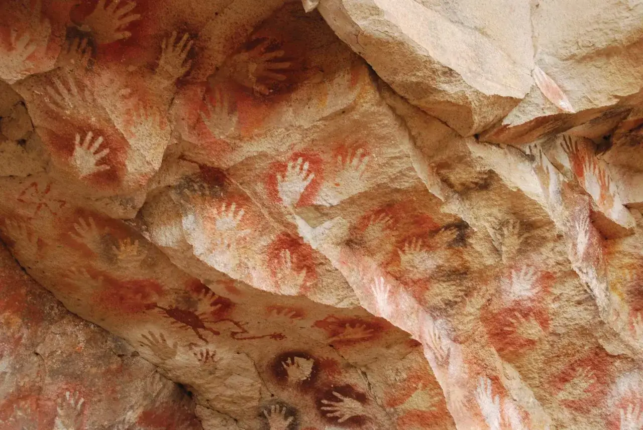Antiche pitture rupestri nella grotta delle mani, con impronte di mani rosse e bianche che decorano le pareti rocciose.