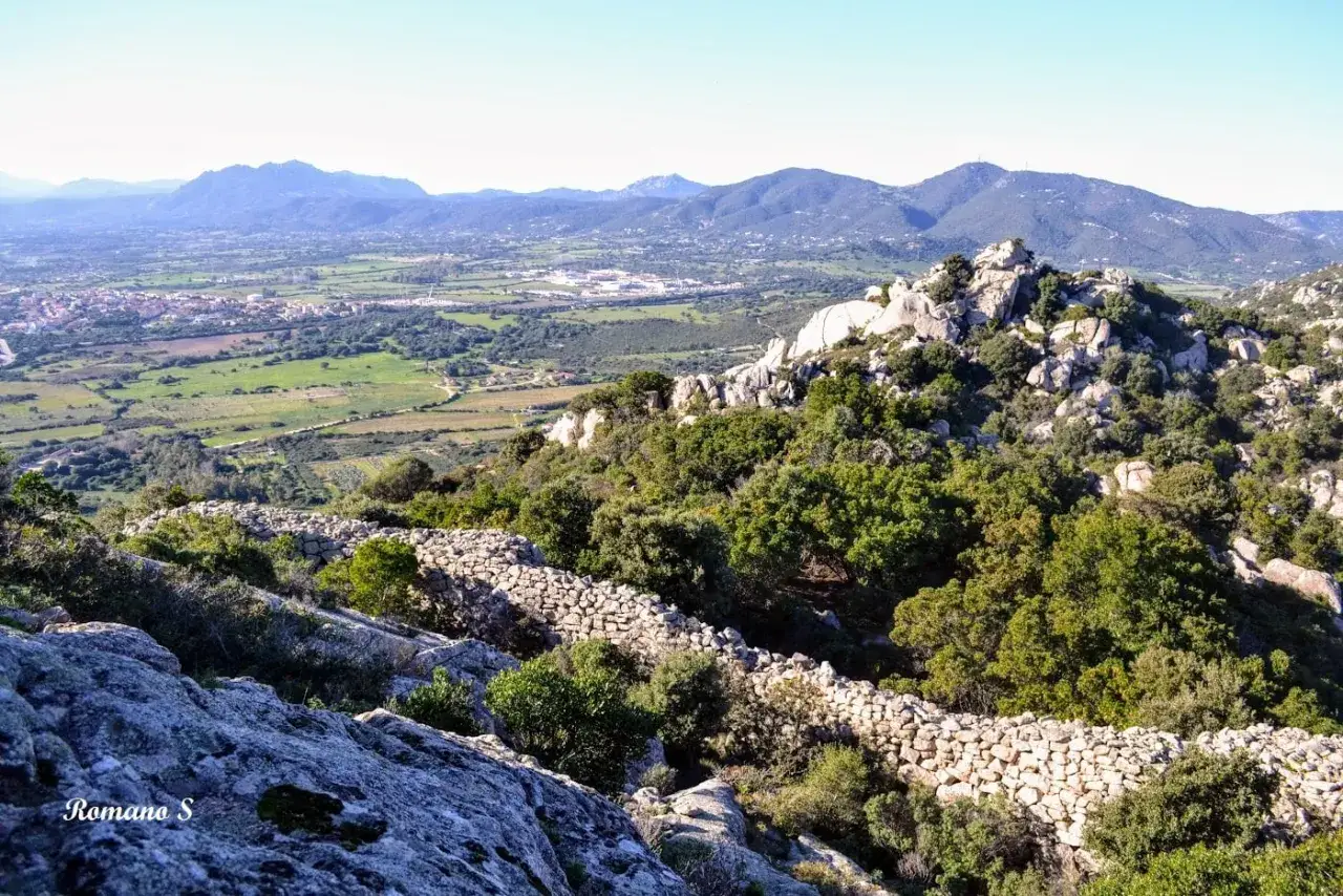Vista panoramica sulla valle con il nuraghe Cabu Abbas, circondato da rocce e vegetazione rigogliosa.