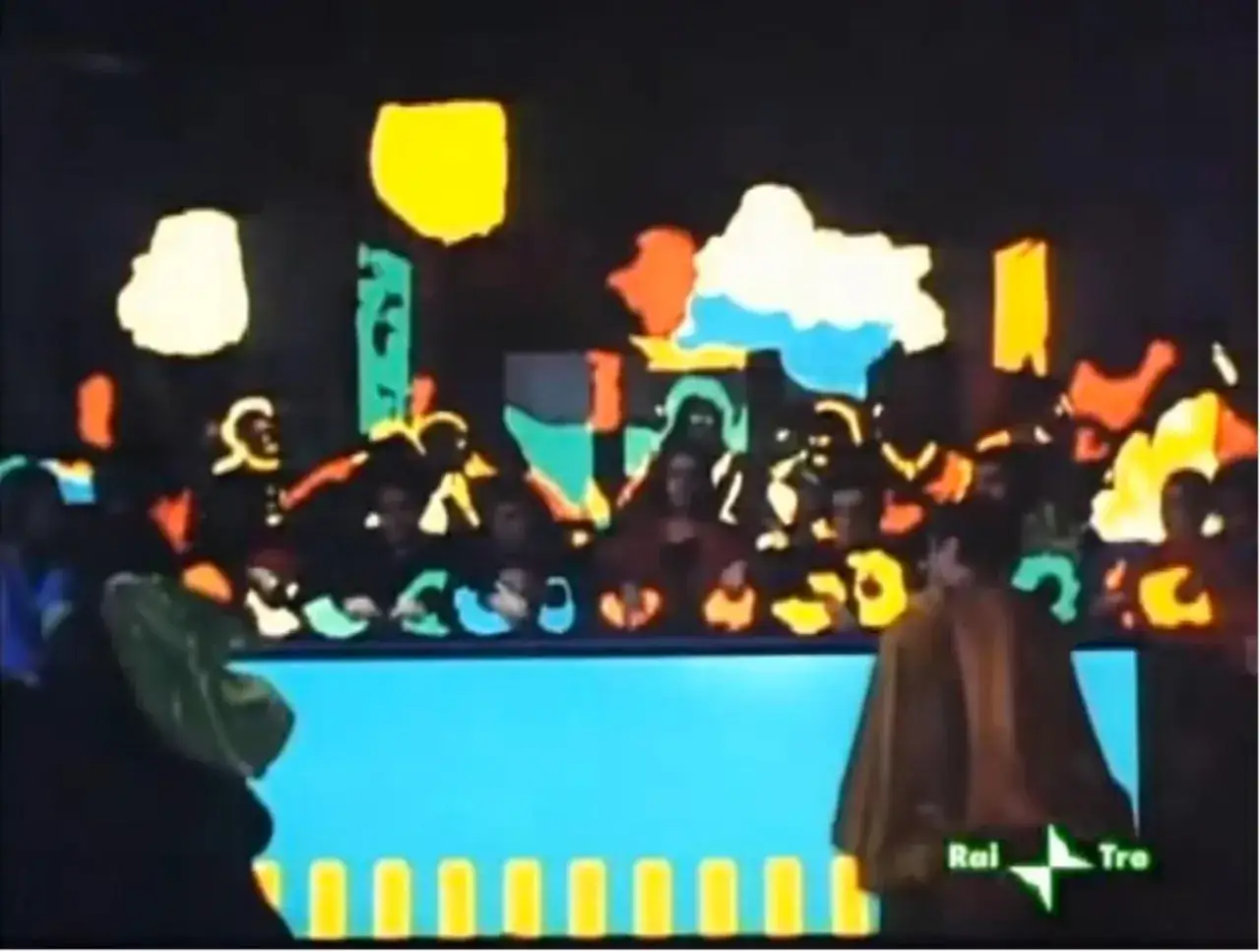 Scena colorata con figure stilizzate. Al centro, un uomo con mantello marrone, forse un riferimento a Salome bene, si volta verso un pubblico vivace.