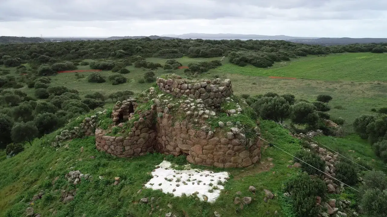Il nuraghe Sirai, imponente struttura in pietra, domina un paesaggio verdeggiante di macchia mediterranea e campi coltivati.