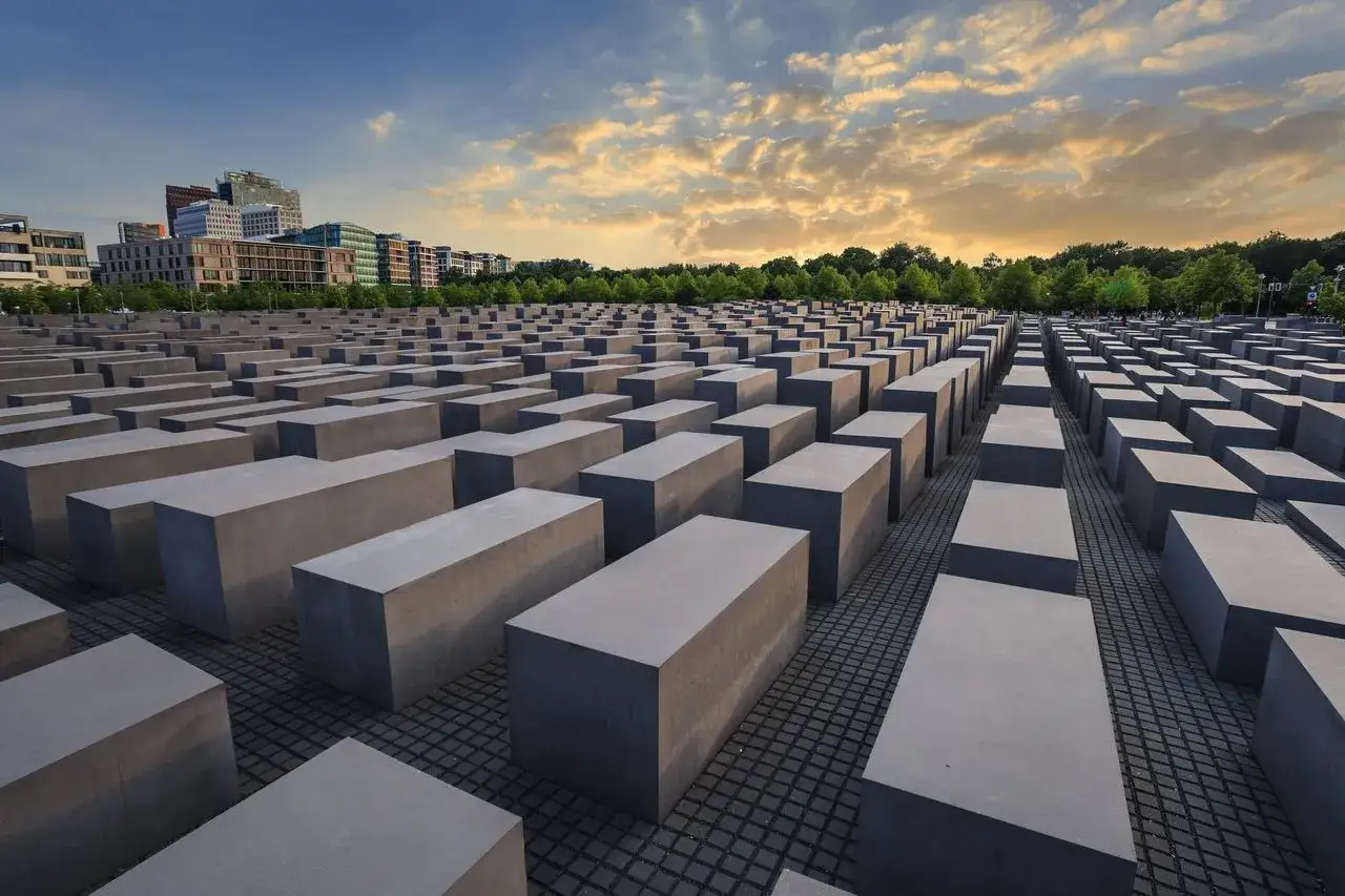 Il memoriale dell'Olocausto a Berlino, un campo di stele di cemento sotto un cielo nuvoloso al tramonto.