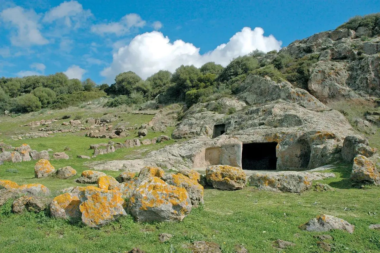 Antico altare rupestre di Santo Stefano, scavato nella roccia, con ingressi scuri e rocce coperte di licheni gialli.