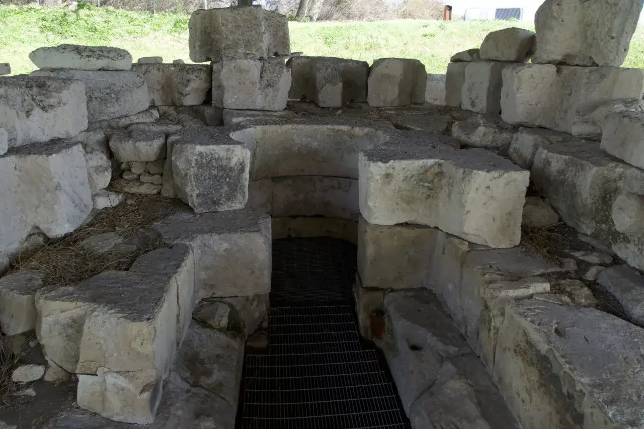 Antico pozzo sacro nuragico, con blocchi di pietra grezza che circondano un'apertura protetta da una grata metallica.