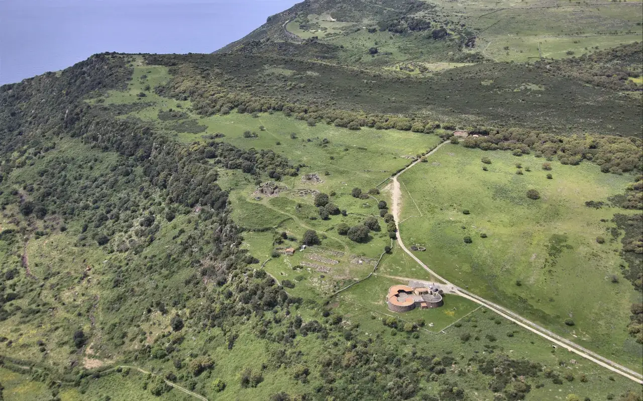 Vista aerea del nuraghe Appiu, un sito archeologico con rovine antiche e un edificio moderno, immerso nel verde della campagna sarda.