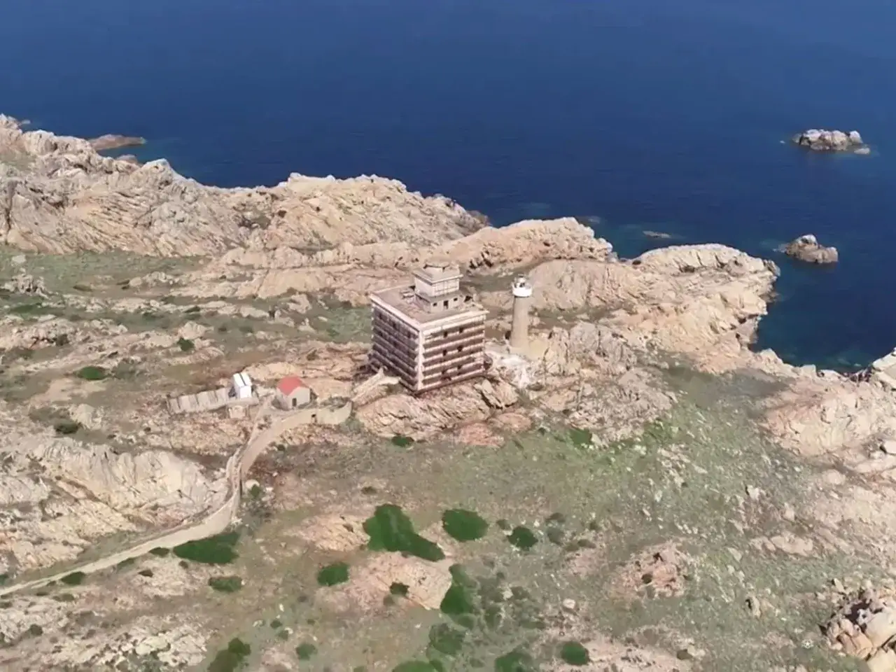 Il faro della Maddalena si erge su una costa rocciosa, con un edificio moderno accanto.