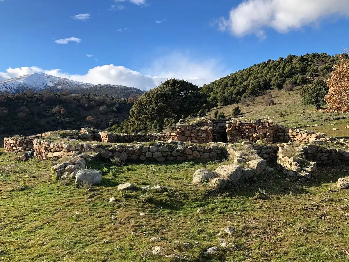 S'arcu e is forros, antiche rovine in pietra su un prato verde, con montagne innevate sullo sfondo.