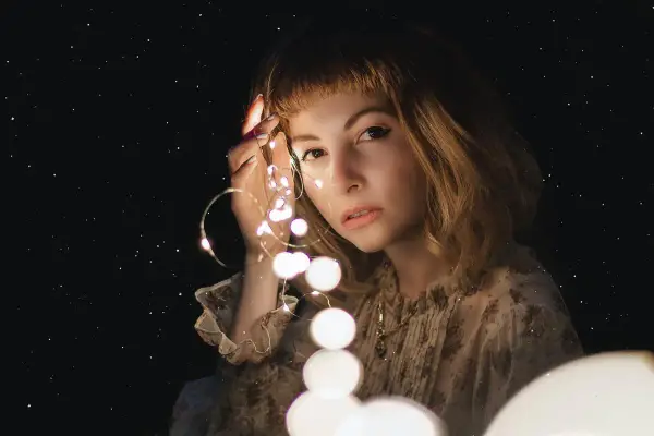 Una ragazza con luci scintillanti tra le dita, come un filo di Arianna che illumina il buio.